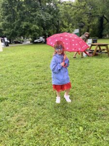 Female child with red umbrella, blue rain jacket and red skirt outside during rain